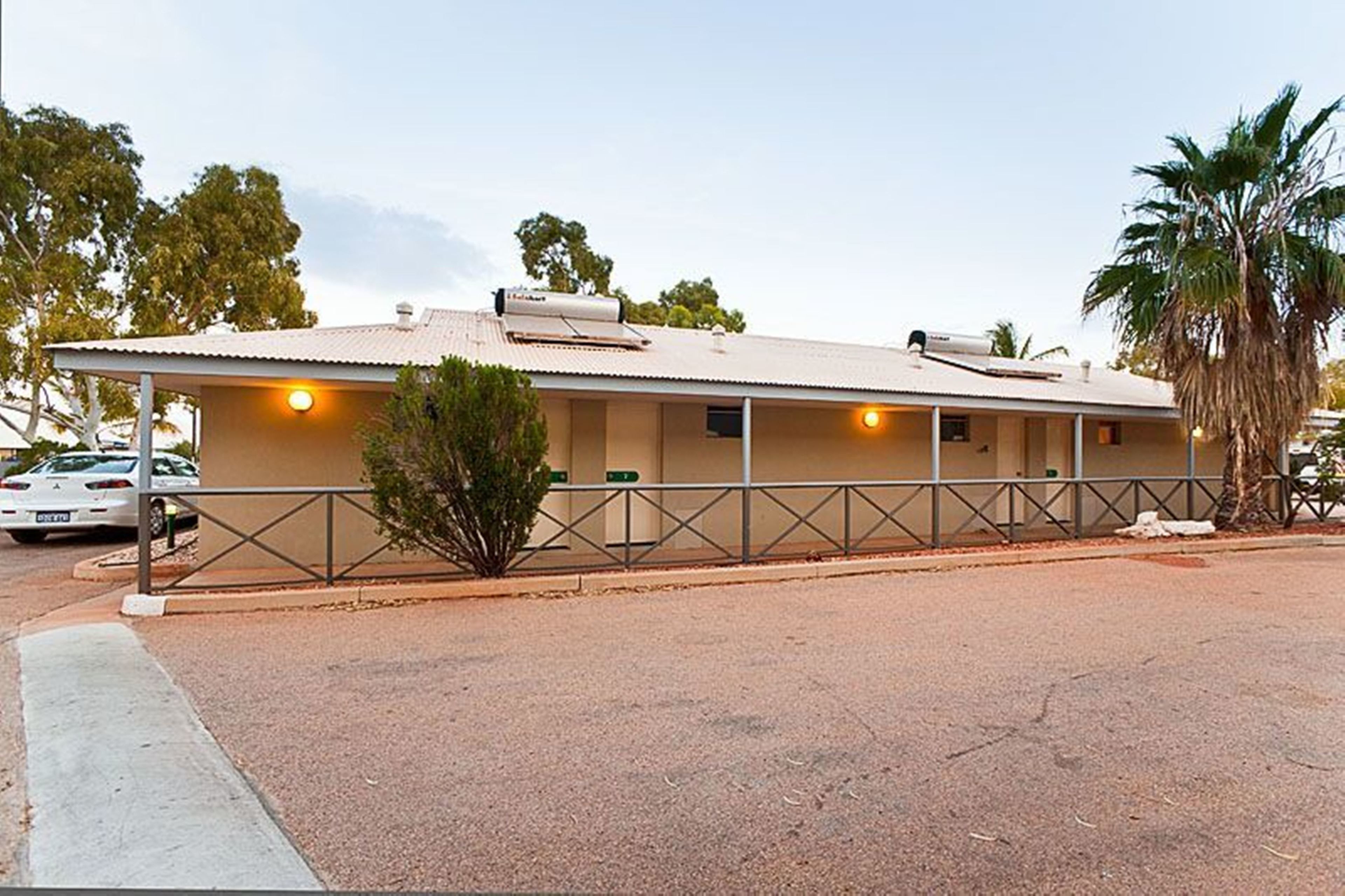 A single-story building with a flat roof, a covered porch, and a fenced parking area.