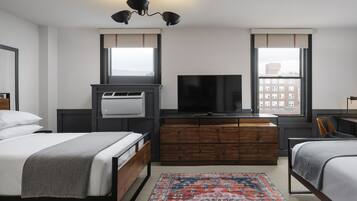Habitación de hotel con cama, televisor, cómoda y ventana con vista a edificios.