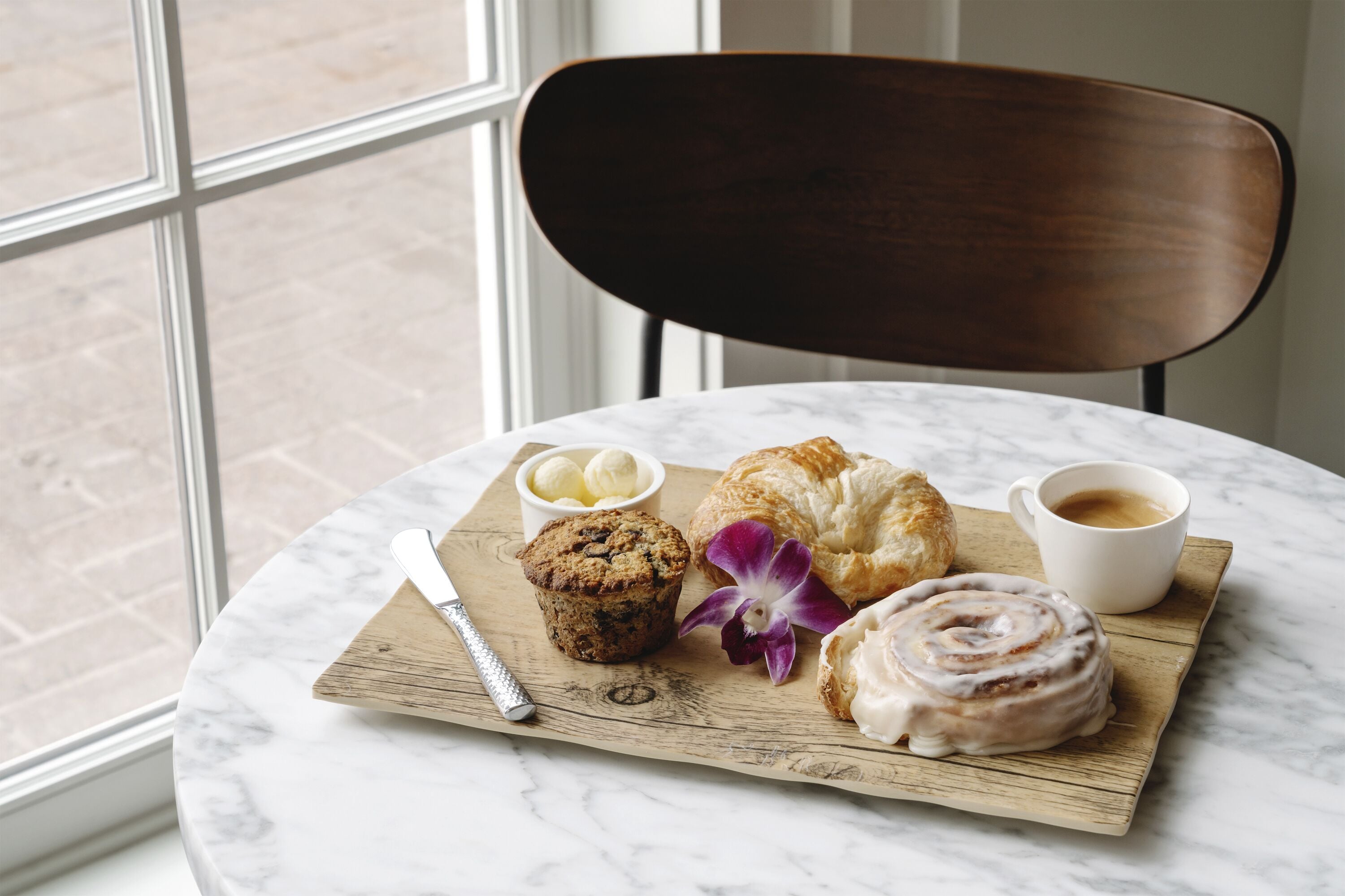 Une table avec un croissant, un muffin et un pain à la cannelle, ainsi qu’une tasse de café et un petit bol de beurre.