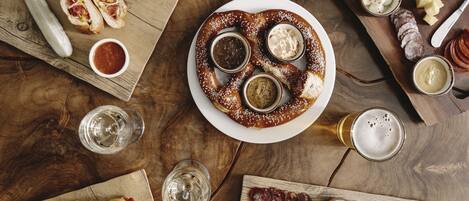 Una mesa de madera con diversos alimentos, como pretzels, carnes, quesos y salsas.