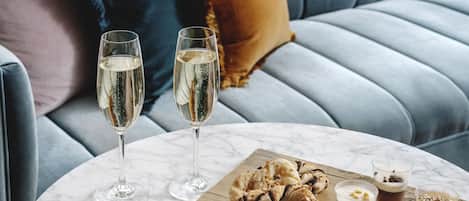 A marble table with two glasses of white wine, a wooden board with pastries, and a bowl of grapes.