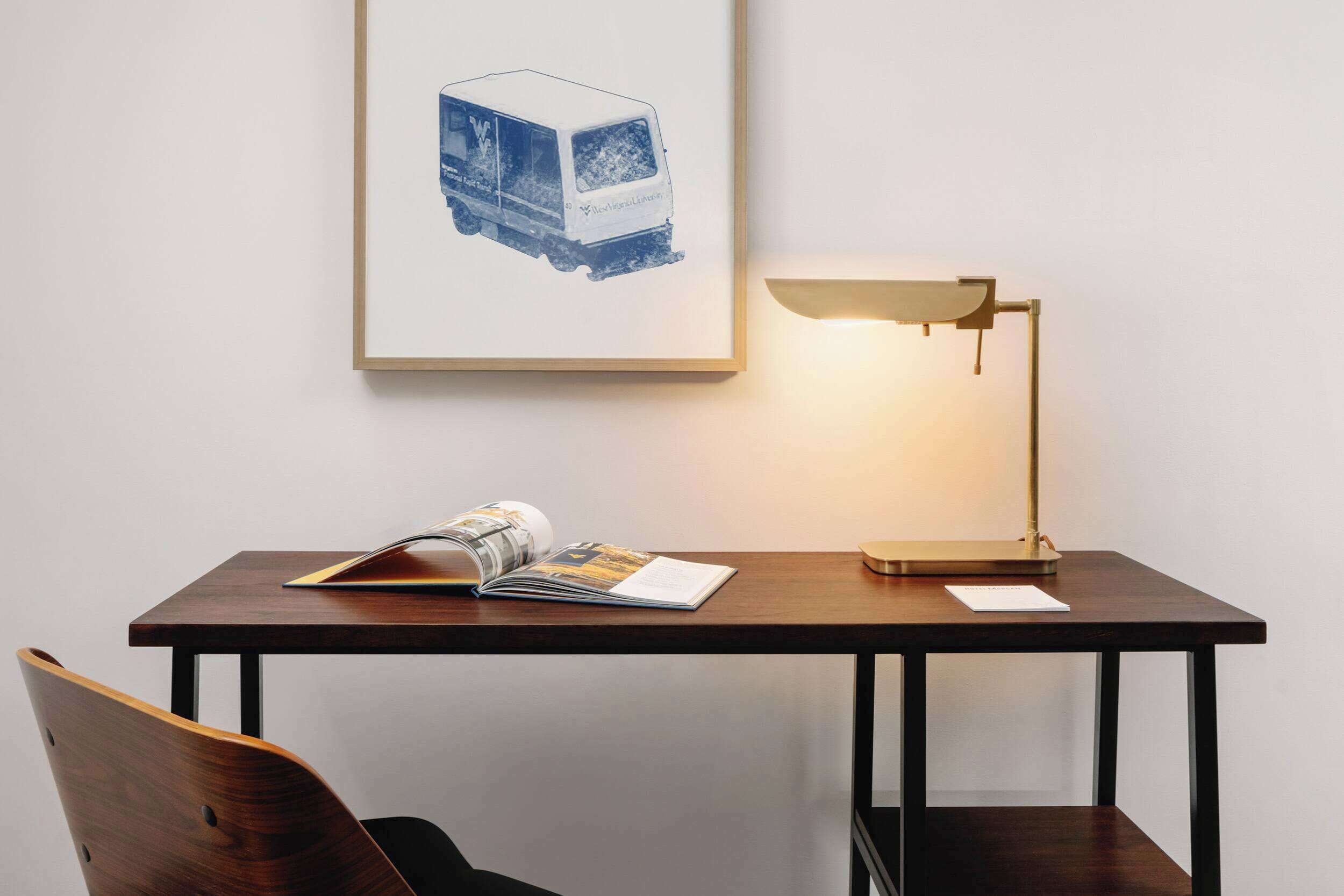 A wooden desk with a lamp, a chair, and a framed picture on the wall.