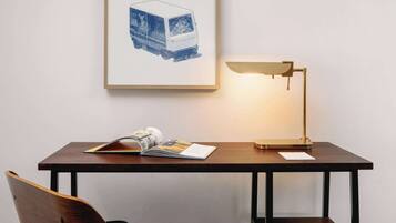 A wooden desk with a lamp, a chair, and a framed picture on the wall.