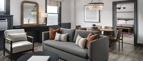 Un salon moderne avec un canapé gris, des fauteuils, une table basse et un lustre.
