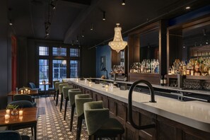 Un espace bar doté d’un long comptoir, de nombreux tabourets et d’un lustre.