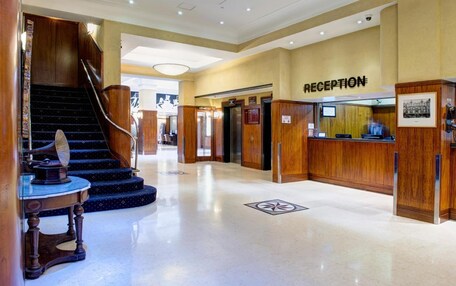 A hotel reception area with a wooden reception desk, a reception sign, and a staircase leading to an upper floor.