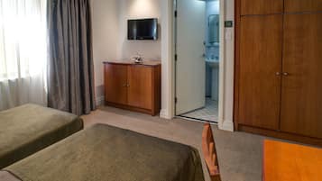 Camera d'albergo con due letti singoli, un armadio in legno, una televisione a parete e un bagno visibile attraverso una porta aperta.