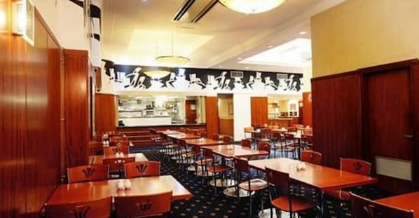 Un restaurante con varias mesas y sillas, paneles de madera en las paredes y una zona de mostrador central.