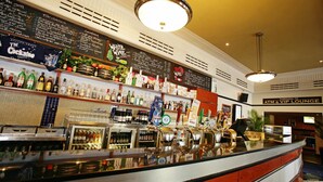 Una zona de bar con mostrador, estantes llenos de botellas de licor y un menú en una pizarra.
