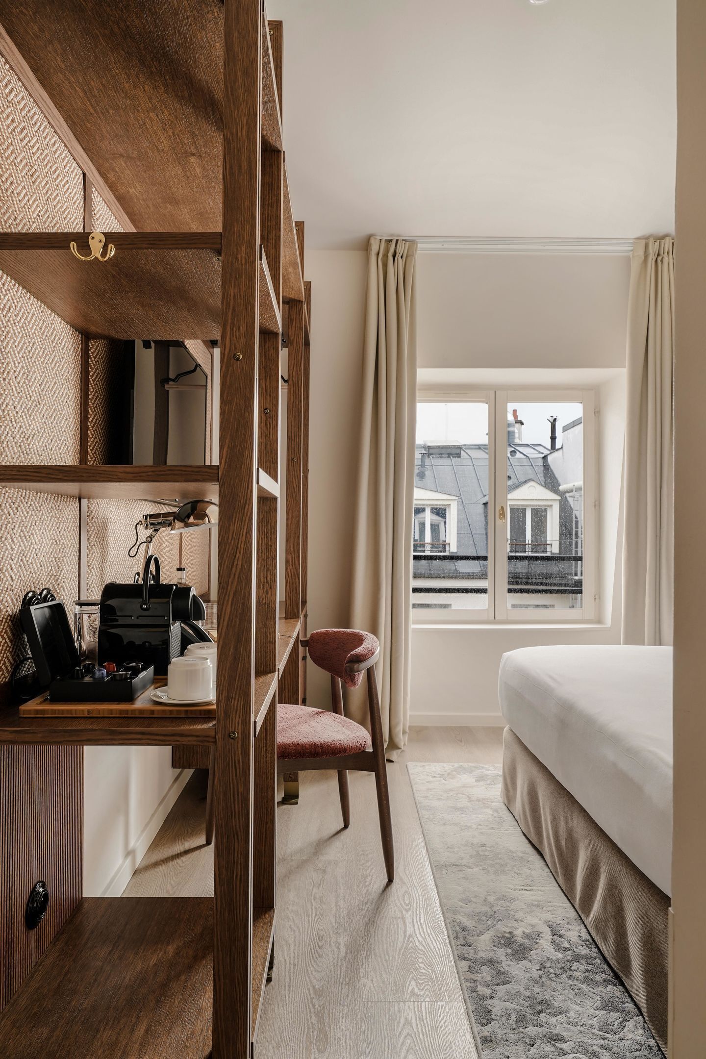 Ein Hotelzimmer mit einem Holztisch, einem Stuhl, einem Bett und einem Fenster mit Blick auf Gebäude.