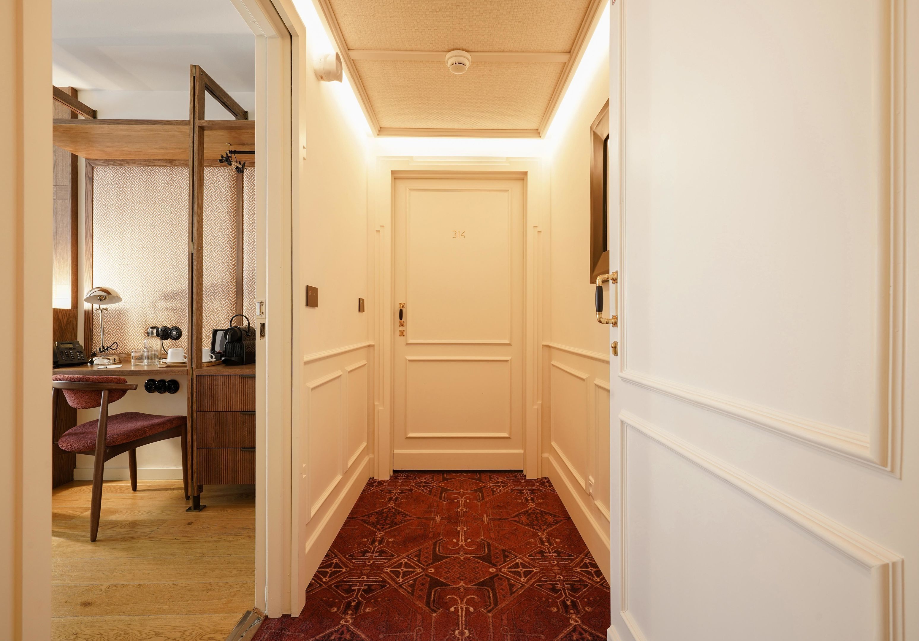 A hallway with a patterned carpet, a wooden desk with a chair, and a door with the number 314.