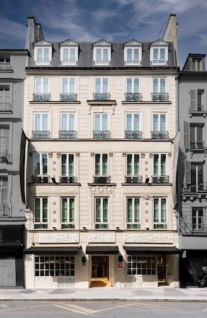 Un hôtel à plusieurs étages, de style architectural européen classique, caractérisé par des balcons symétriques et une entrée centrale dotée d’une porte en verre.