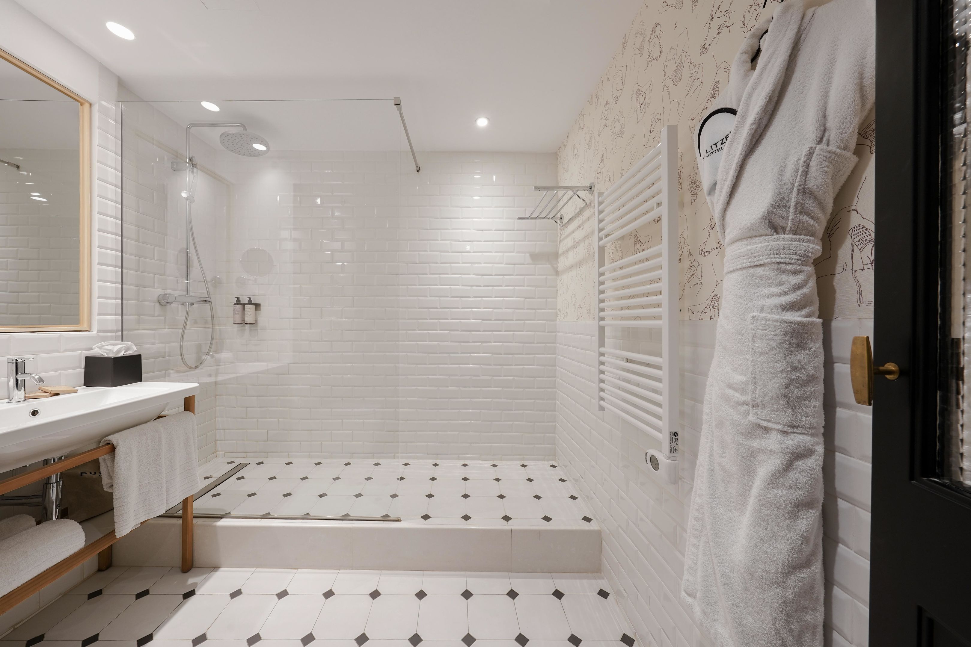 Un baño moderno con azulejos blancos tipo metro, una ducha con cerramiento de vidrio, un lavabo blanco y un perchero para toallas.