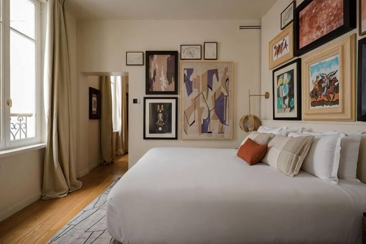 A bedroom with a large bed, artwork on the walls, and a window with curtains.