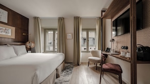 A hotel room with a large bed, a desk with a chair, a television, and a window with curtains. - Hotel Pulitzer Paris (Paris)