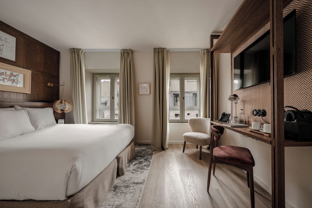 A hotel room with a large bed, a desk with a chair, a television, and a window with curtains.