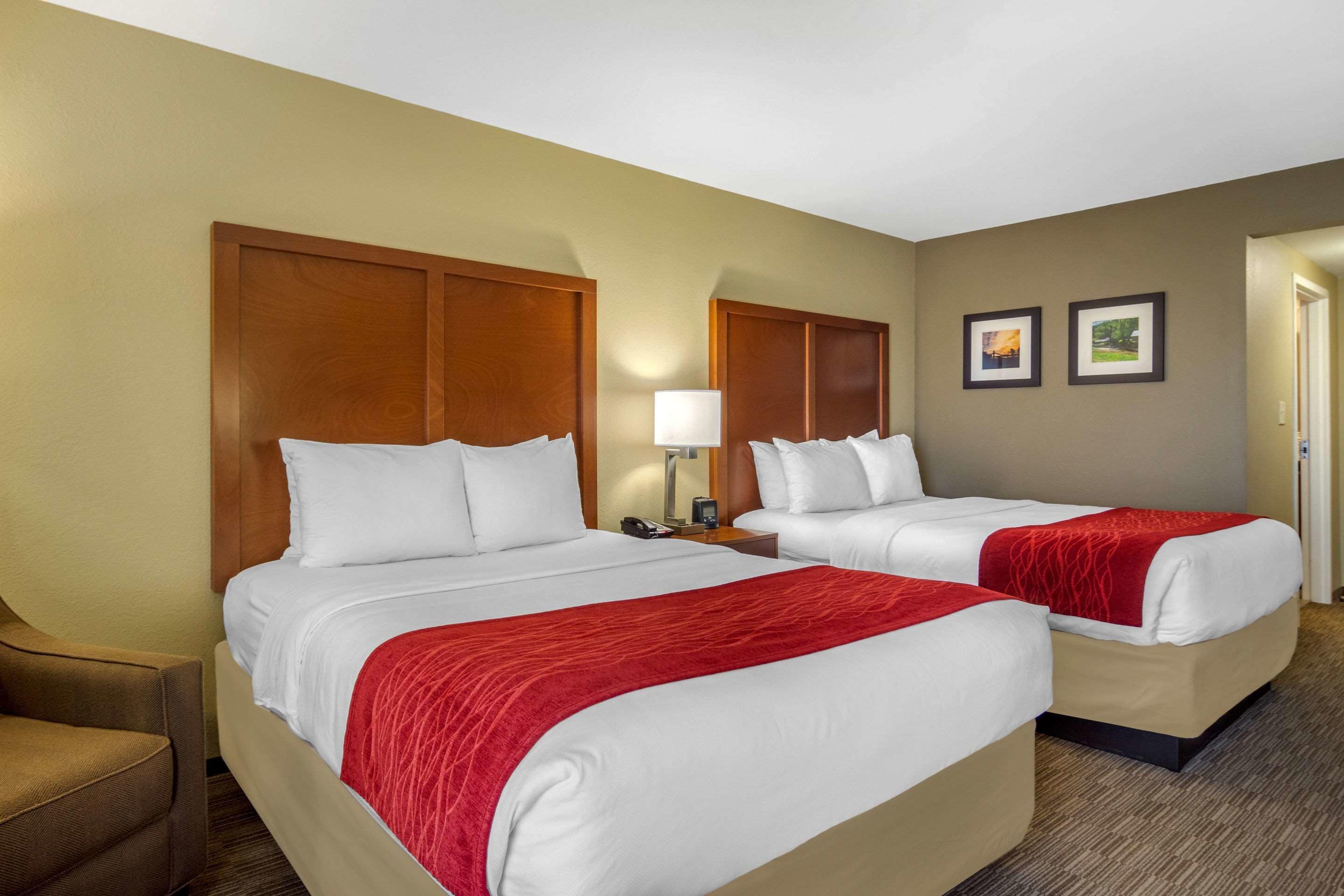 A hotel room with two beds, a chair, a lamp, and two framed pictures on the wall.