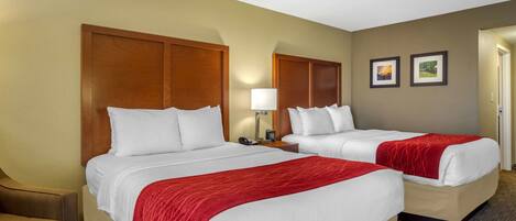 A hotel room with two beds, a chair, a lamp, and two framed pictures on the wall.