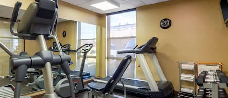 Un gimnasio con máquinas de cardio, bancos de pesas y mancuernas.