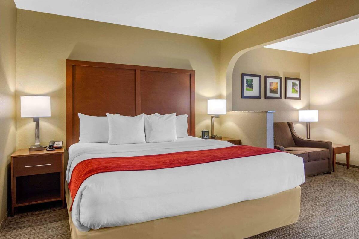 A hotel room with a large bed, two bedside tables with lamps, a chair, and a wall with framed pictures.