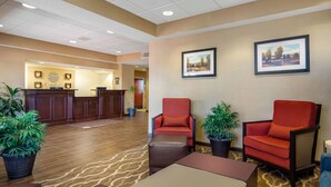 A hotel lobby with a reception desk, two red armchairs, a brown ottoman, and potted plants. - Comfort Inn & Suites LaGrange East (LaGrange)