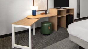 A hotel room with a bed, a desk with a lamp, a television, and a trash bin.
