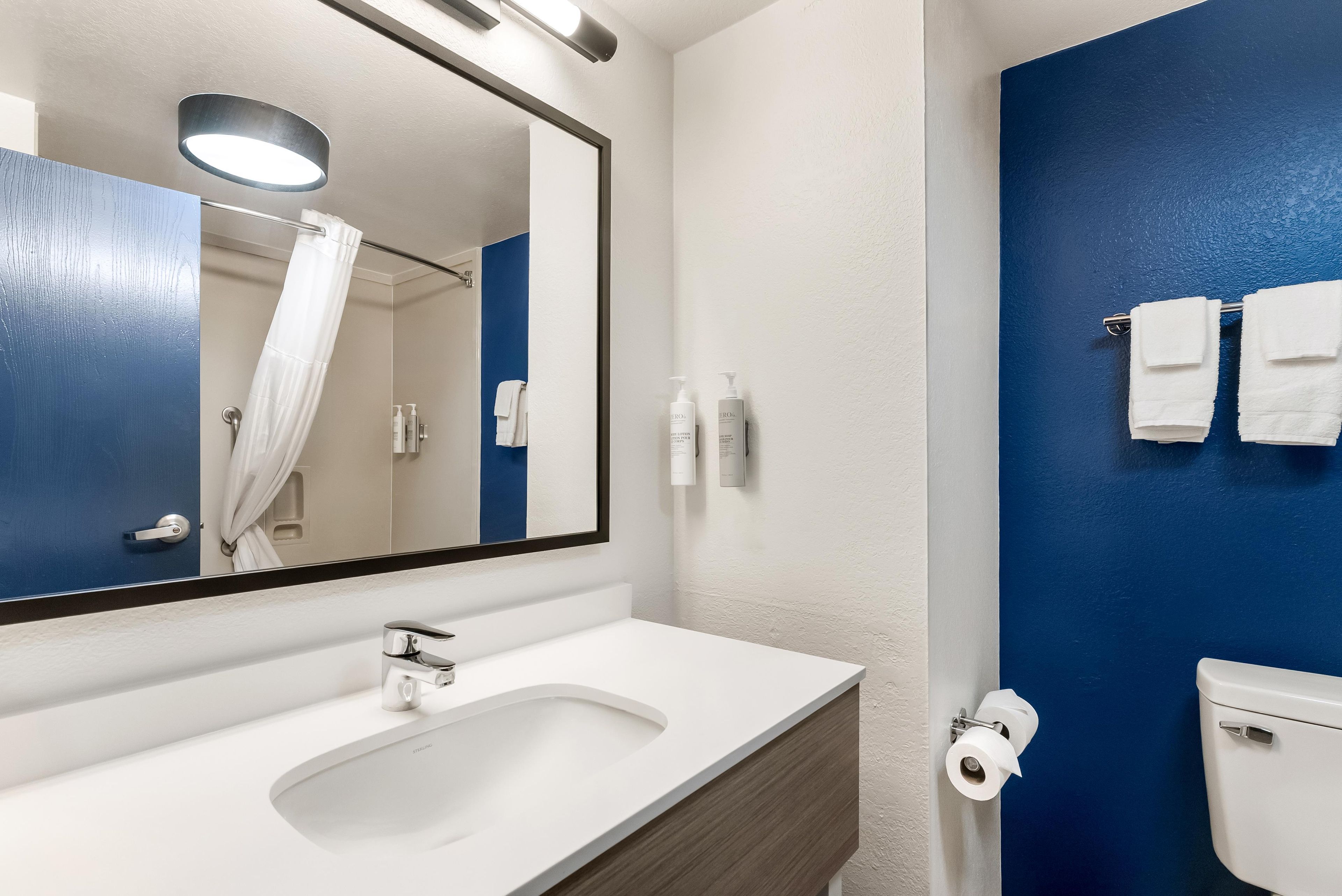 Une salle de bain avec un lavabo blanc, un miroir, un mur bleu et des toilettes.