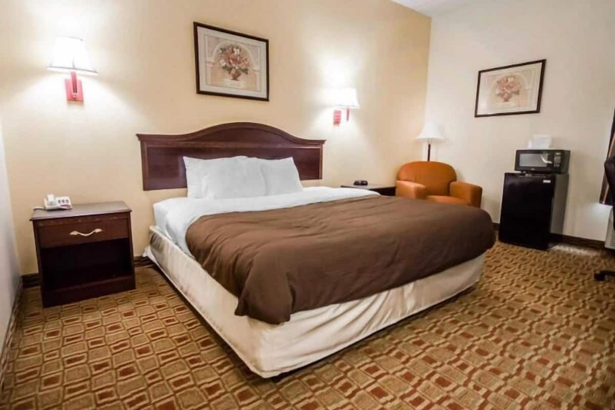 A hotel room with a bed, a nightstand, a chair, a desk with a computer, and a microwave.