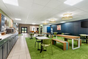 Une cafétéria moderne avec un revêtement de sol en gazon synthétique vert, des tables et des chaises en bois.