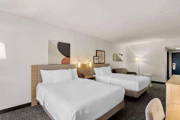 Une chambre d’hôtel avec deux lits, un bureau, une chaise et une table de chevet avec une lampe.
