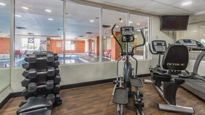A gym with exercise equipment, large windows, and a pool area visible through the windows. - Comfort Suites Richmond (Richmond)