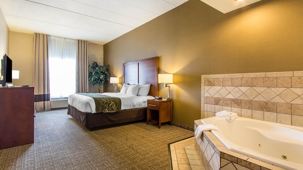 Una habitación de hotel con cama, mesita de noche, lámpara y una bañera.