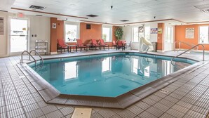 Una piscina interior con agua cristalina, rodeada de sillas rojas y un suelo de baldosas.