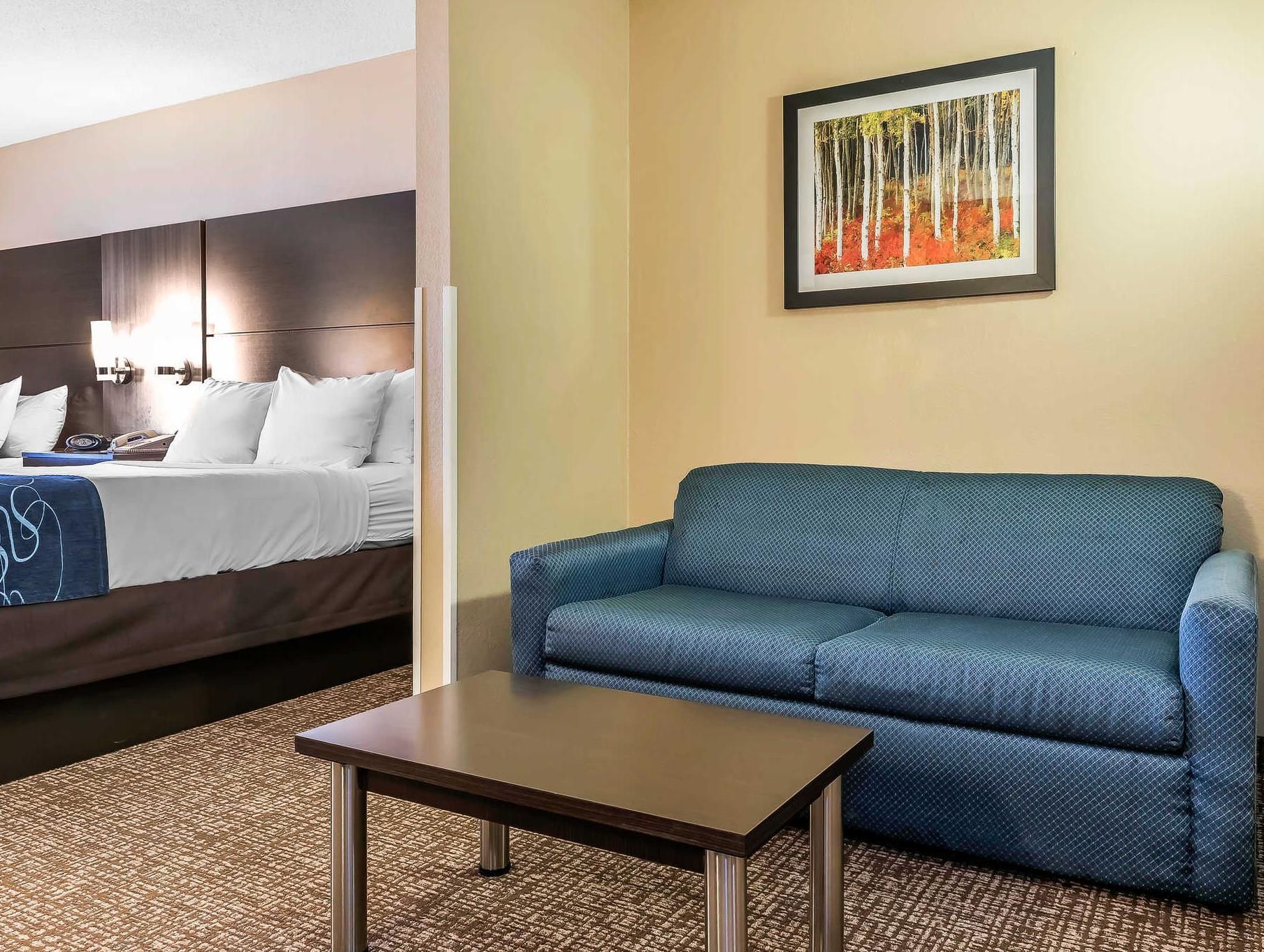 Een hotelkamer met een bed, een blauwe bank, een klein tafeltje en een lijst met een afbeelding aan de muur.