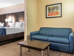 Una habitación de hotel con una cama, un sofá azul, una mesita y un cuadro en la pared.