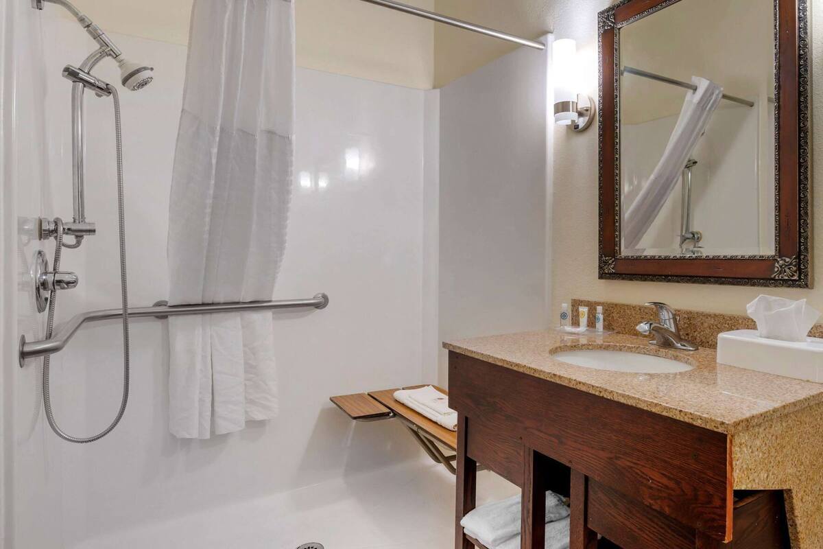A bathroom with a shower, a vanity with a sink, a mirror, and a towel rack.