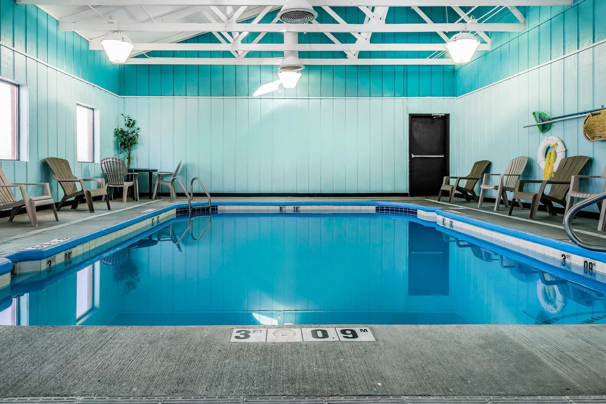 An indoor swimming pool with a blue tiled floor, a ceiling fan, and chairs around the pool.