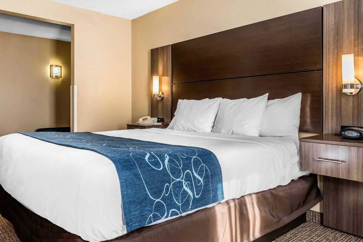 A hotel room with a large bed, bedside tables, a nightstand, and wall-mounted lights.