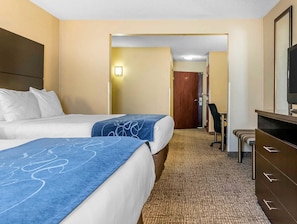 Habitación de hotel con dos camas, un escritorio, una silla, un televisor y una puerta que da a otra habitación.