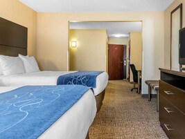 Habitación de hotel con dos camas, un escritorio, una silla, un televisor y una puerta que da a otra habitación.