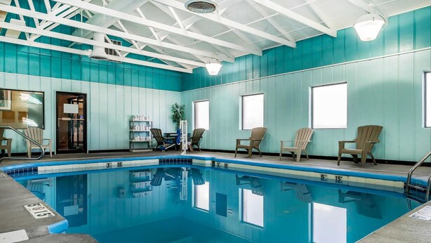 A swimming pool with clear water, surrounded by teal walls and white beams. There are chairs and a small table near the pool, and a door leading to another room. - Comfort Suites Miamisburg - Dayton South (Miamisburg)