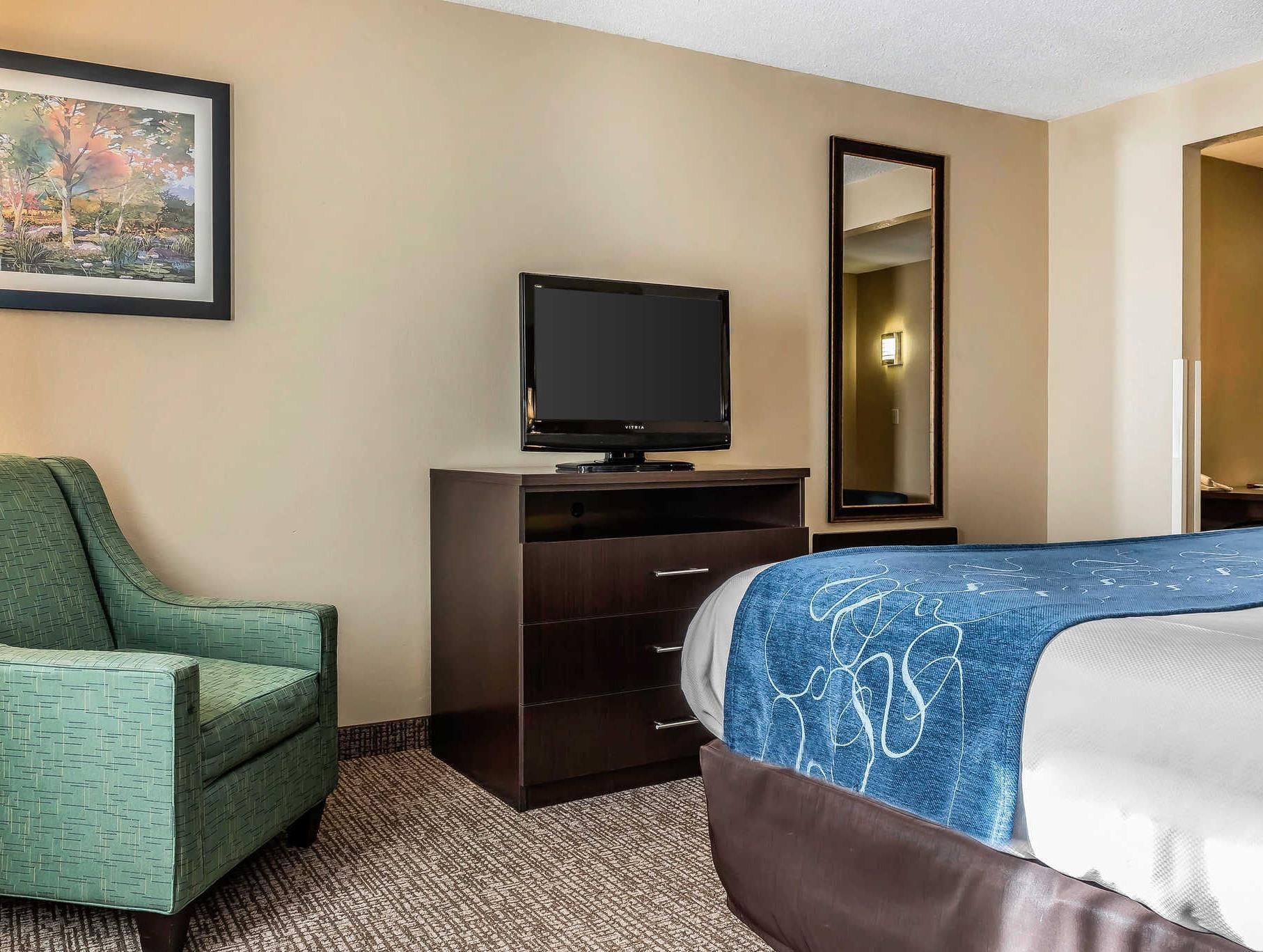 A hotel room with a bed, a television, a chair, a dresser, and a painting on the wall.
