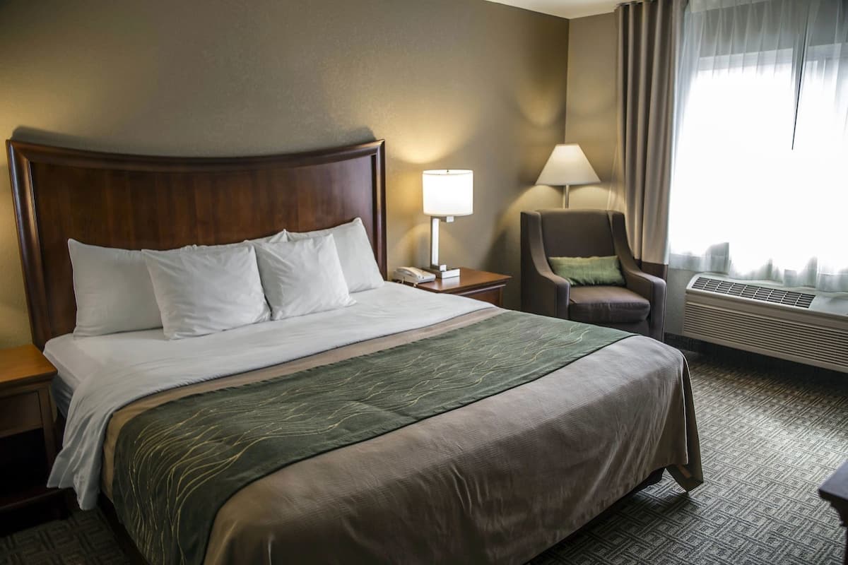 Una habitación de hotel con una cama grande, una silla, una lámpara y un equipo de aire acondicionado.