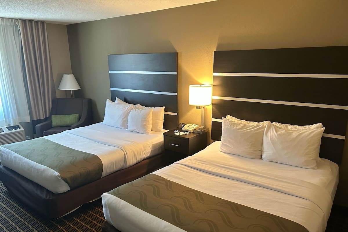 Una habitación de hotel con dos camas, un escritorio, una silla y una lámpara.