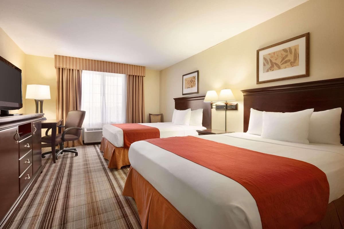 A hotel room with two beds, a desk, a TV, and a chair.