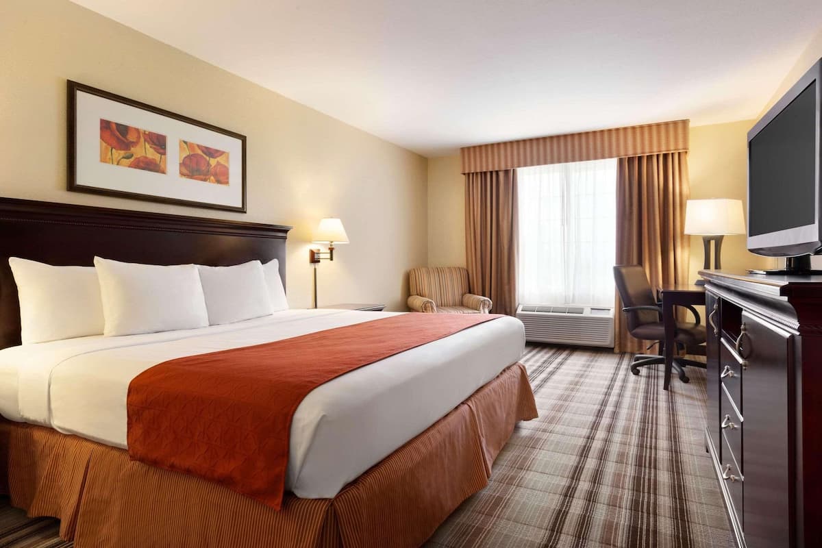 A hotel room with a large bed, a desk with a TV, a chair, and a window with curtains.