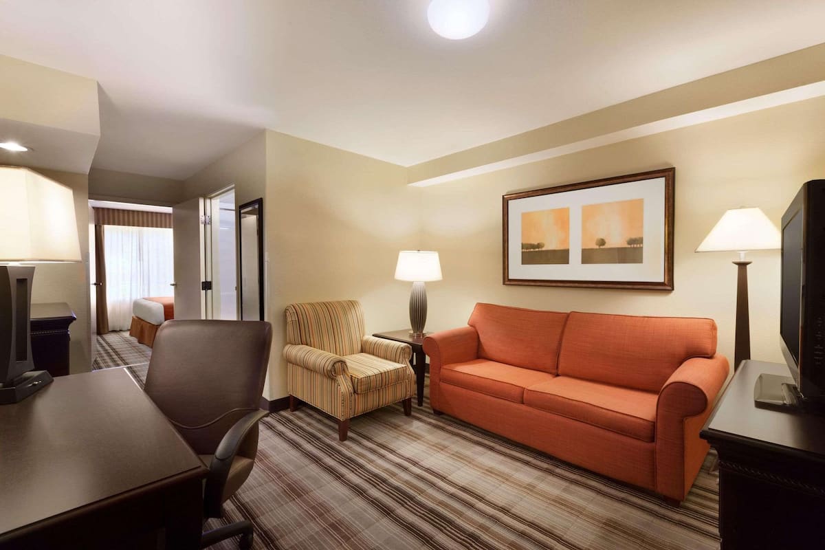 A hotel room with a striped armchair, an orange sofa, a TV, and a framed picture on the wall.