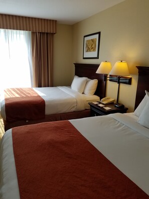 A hotel room with two beds, a nightstand with a telephone, and a wall-mounted lamp.