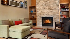 A living room with a stone fireplace, a sofa, a chair, and a bookshelf. - Country Inn & Suites by Radisson, Lexington, VA (Lexington)