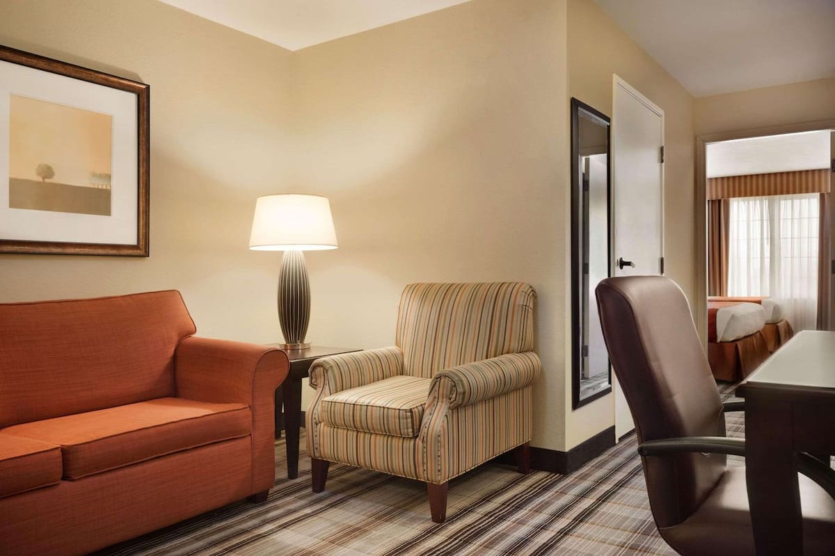 A hotel room with a striped armchair, a sofa, a table, and a lamp.